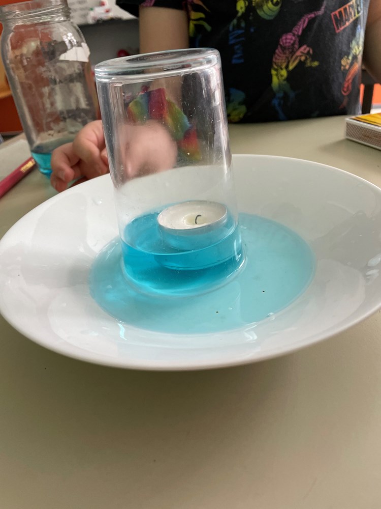 En tallerken med væske, et telys står inni et glass oppå tallerkenen