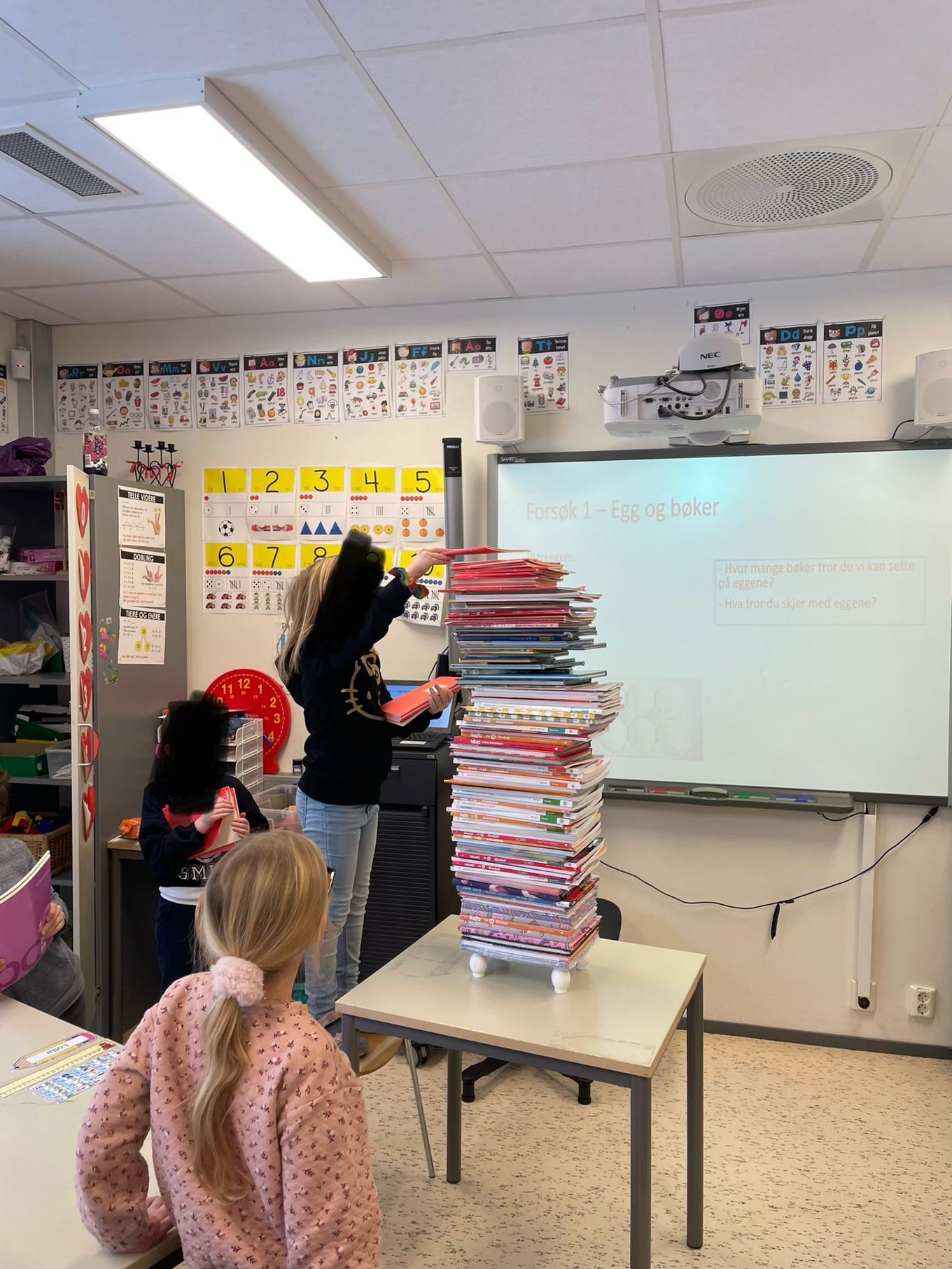 Et barn plasserer et tårn av bøker oppå fire små flasker