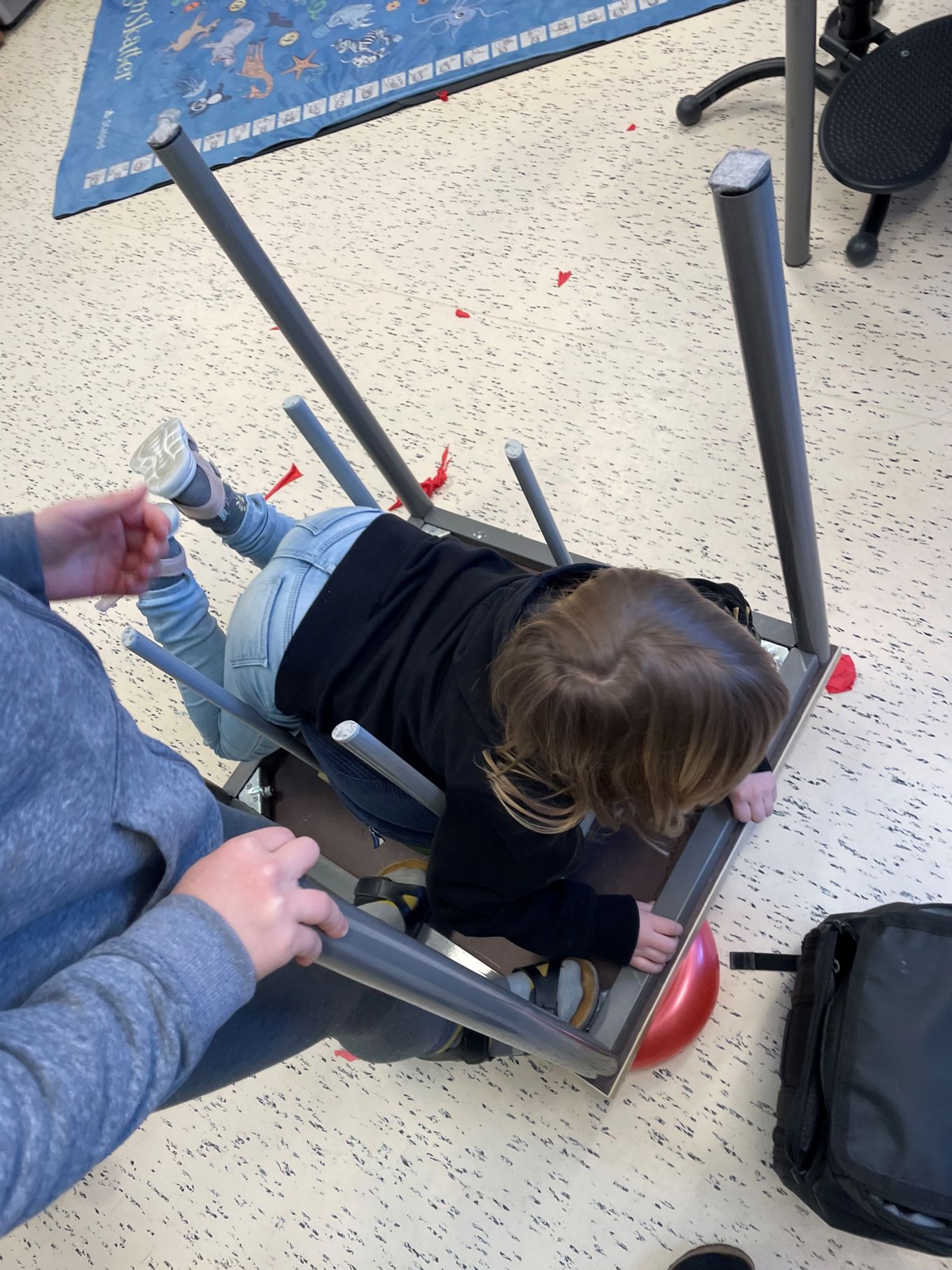 To barn står og ligger oppå en pult som ligger opp-ned på fire ballonger