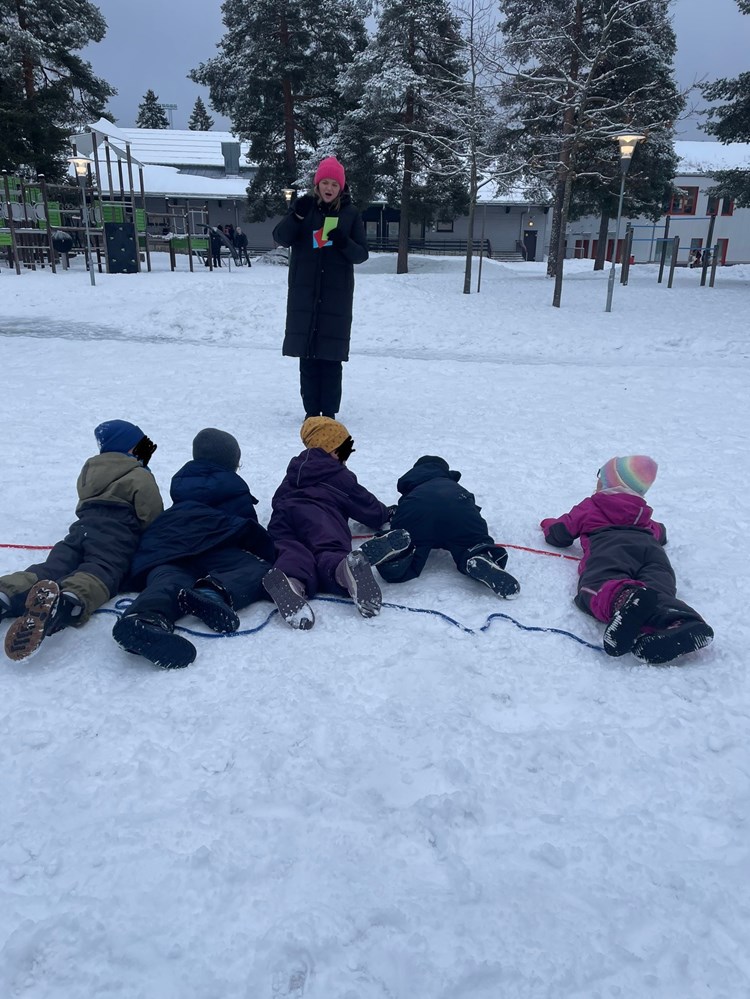 En gruppe barn som ligger i snøen og får instruksjoner av lærer