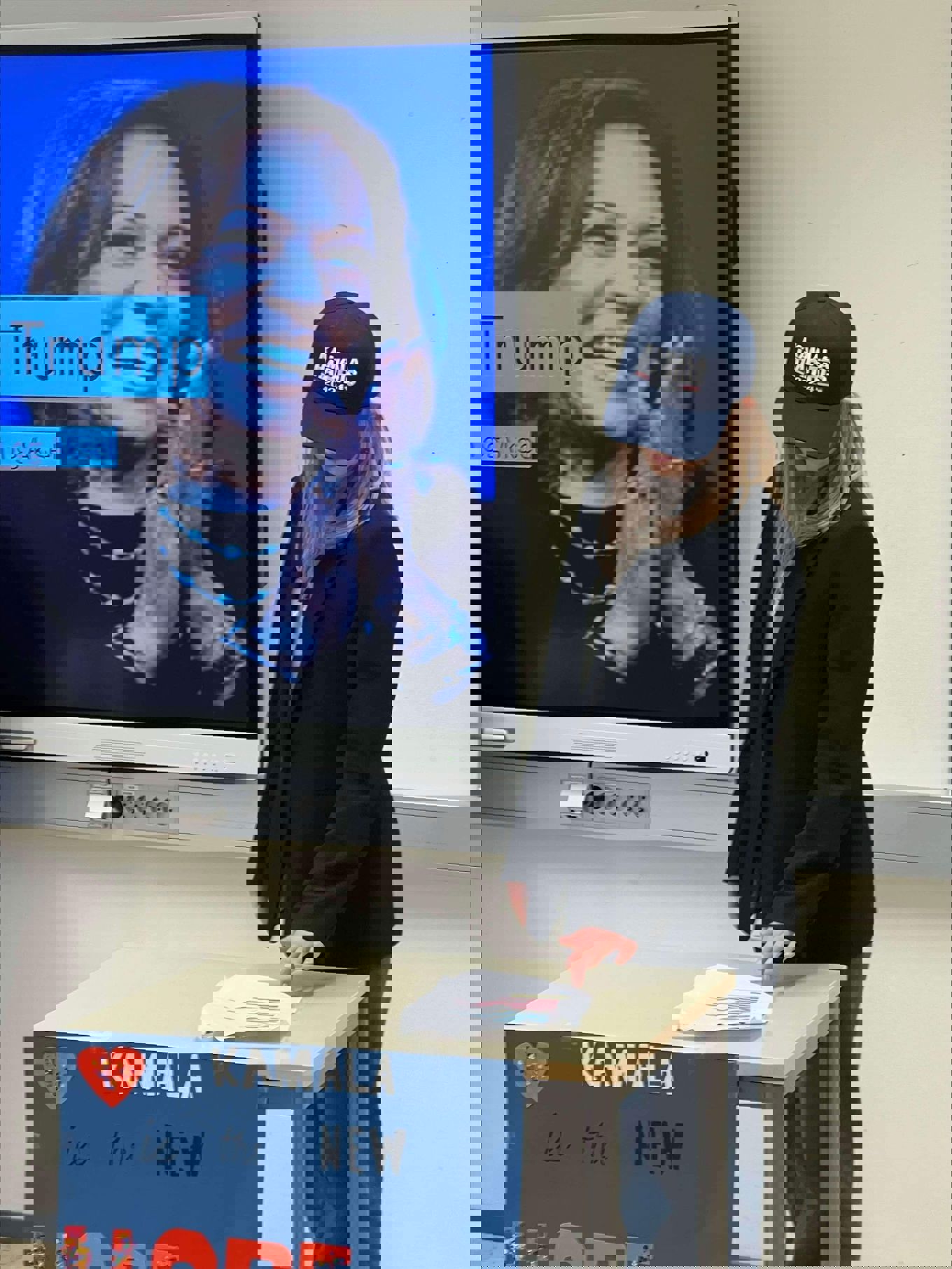 En jente som står ved en pult med et skilt hvor det står "Kamala is the new hope"