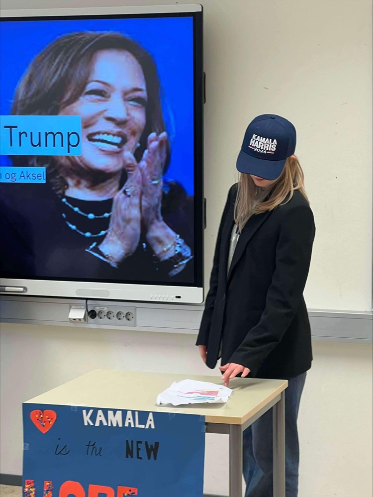 En jente som står ved en pult med et skilt hvor det står "Kamala is the new hope"