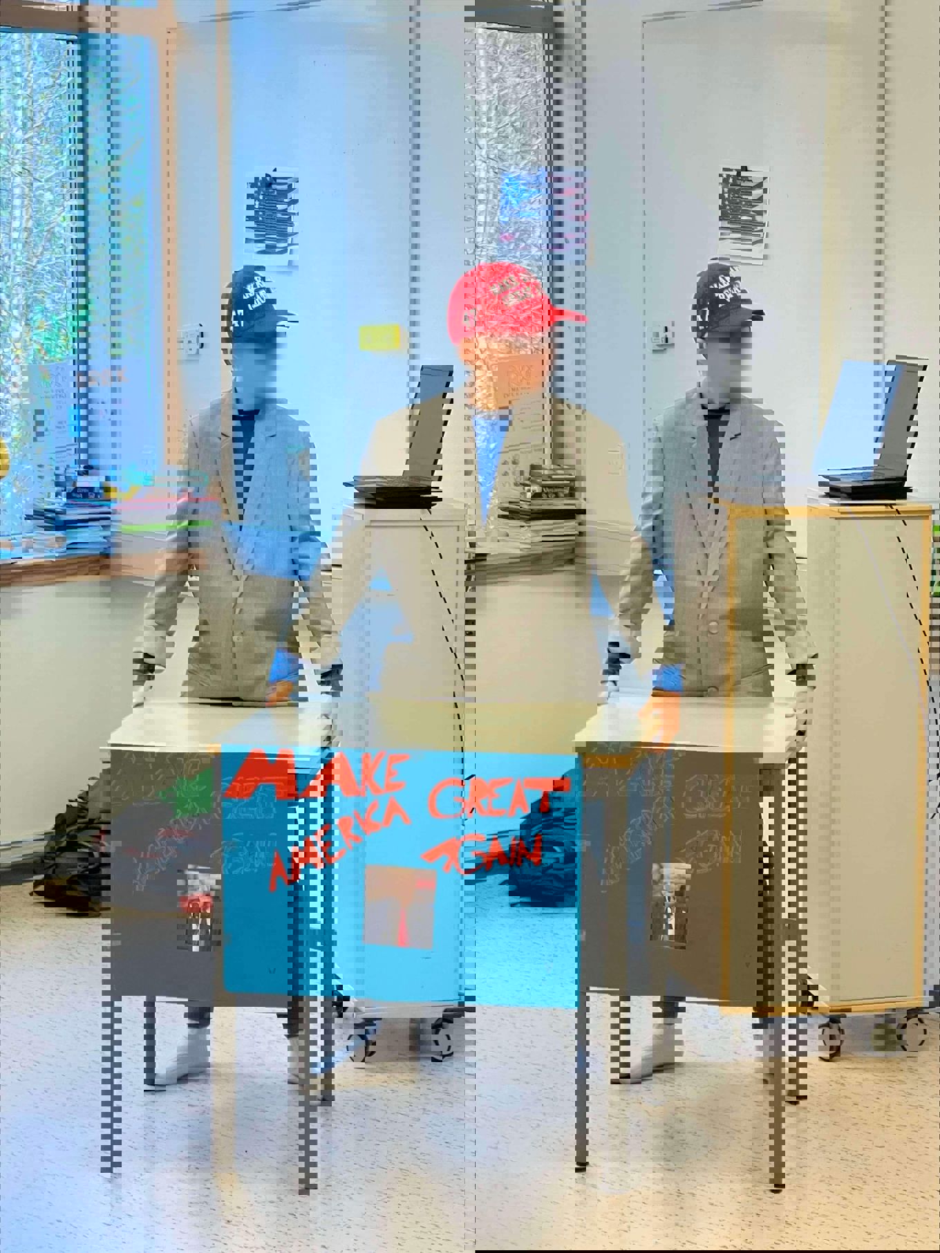 En gutt som står ved et skrivebord med en plakat av Trump hvor det står "Make America Great Again"